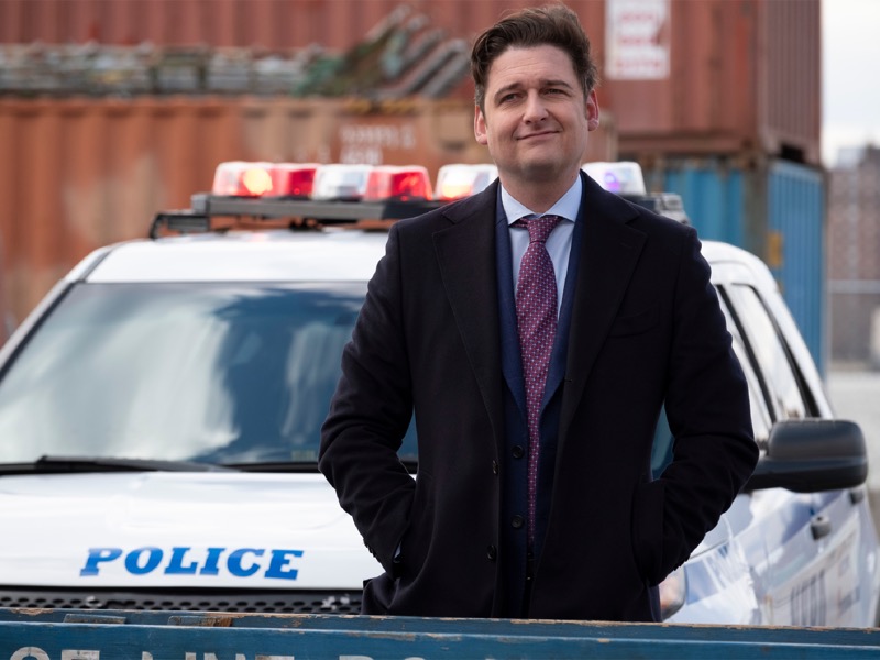 Bryan Connerty from Showtime's Billions standing in front of a police car