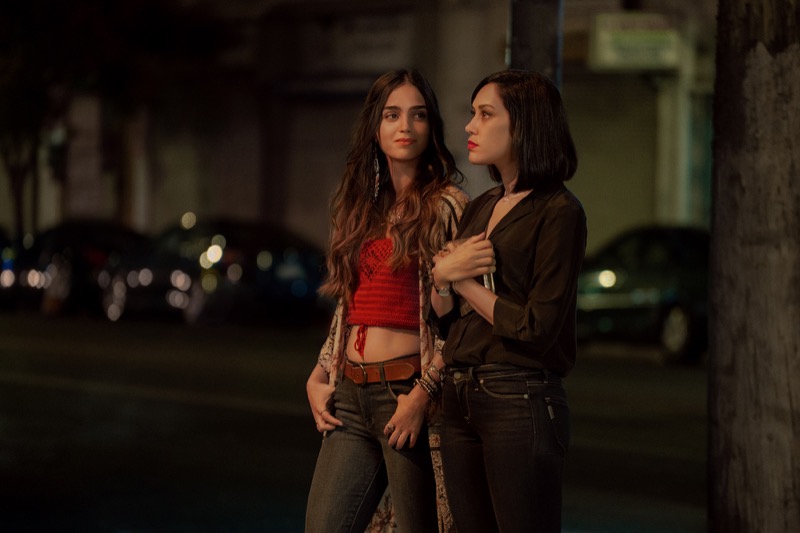 Emma (played by Mishel Prada) and Lyn (played by Melissa Barrera) stand on the sidewalk at night in Vida Season 2