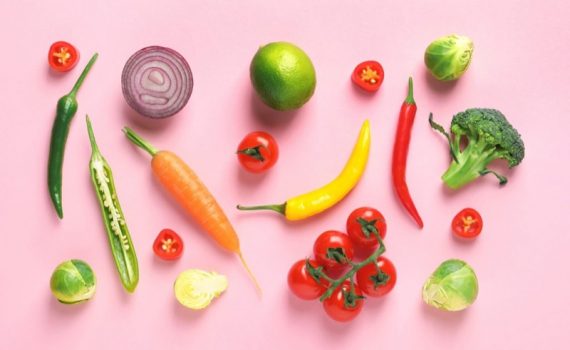 colorful fruits and vegetables laid out on a pink background in a kitchen
