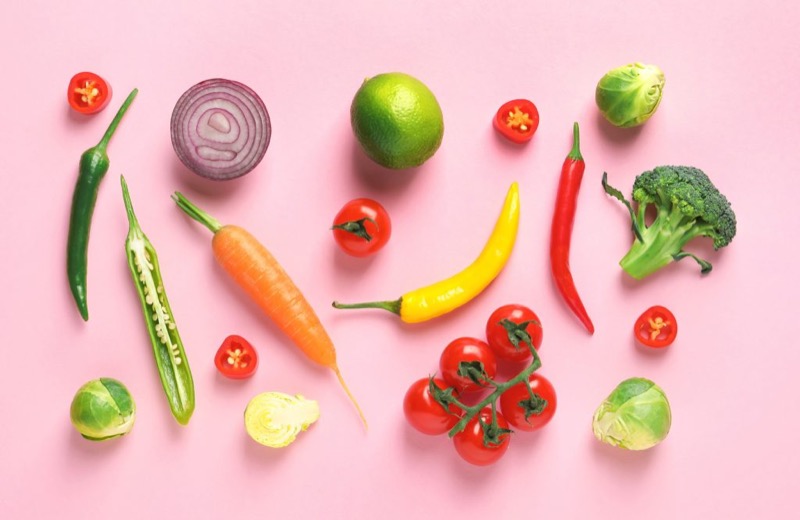 colorful fruits and vegetables laid out on a pink background in a kitchen
