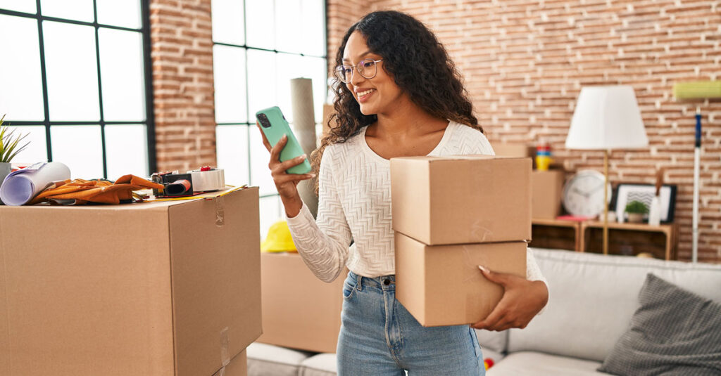 Woman holding some moving boxes looking at a phone